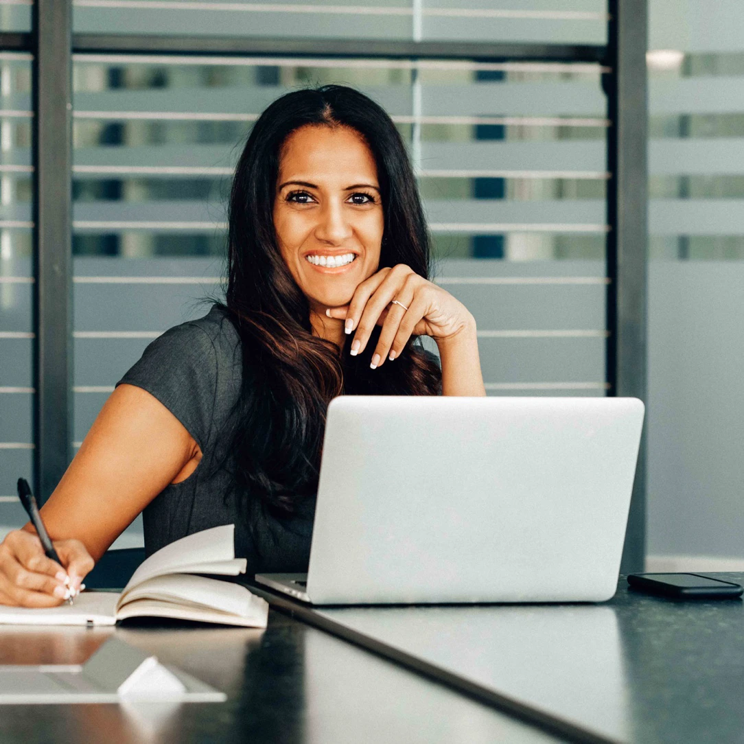 Lächelde Frau mit Stift hinter einem Laptop sitzend